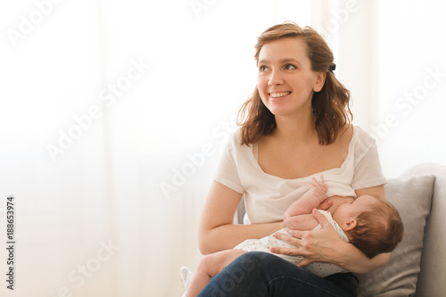 Cheerful young woman breastfeeding infant child at home.  photo