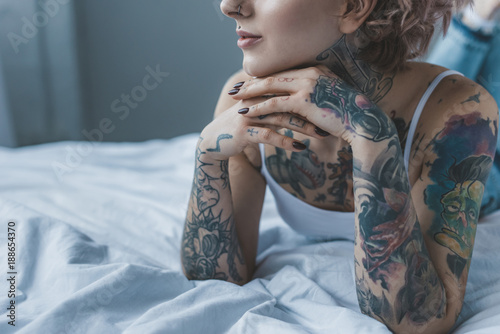 cropped view of dreamy tattooed girl lying on bed photo