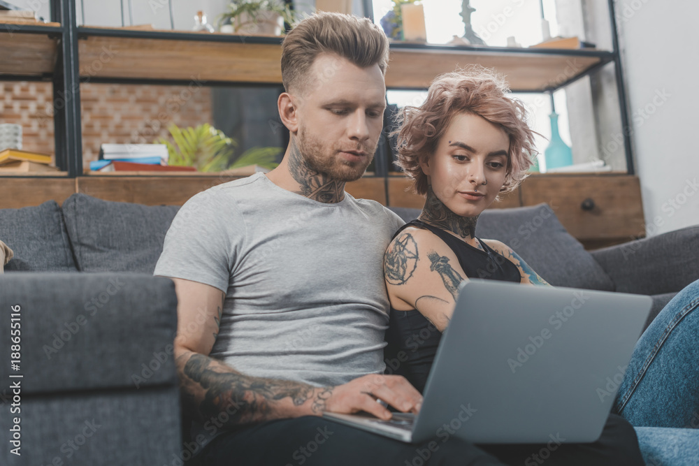 attractive tattooed couple using laptop on sofa at home