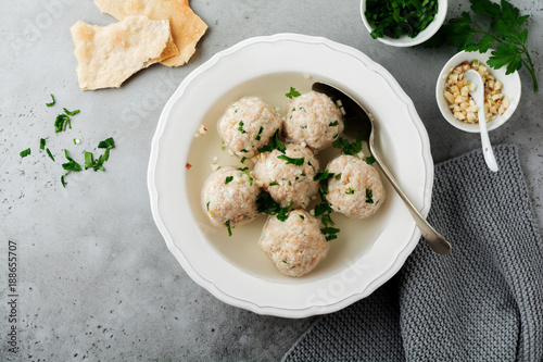 Homemade chicken matzo ball soup with parsley and garlic in simple white ceramic plate on a gray stone or concrete background.  Traditional Jewish passover dish. Selective focus. Top view. photo