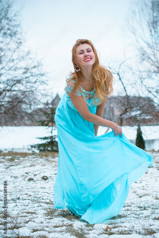 Young beautiful woman in long light blue romantic dress at winter background. Fairy tale girl on winter landscape, elegant lady in the field Young beautiful woman in long light blue romantic dress at winter background. Fairy tale girl on winter landscape, elegant lady in the field