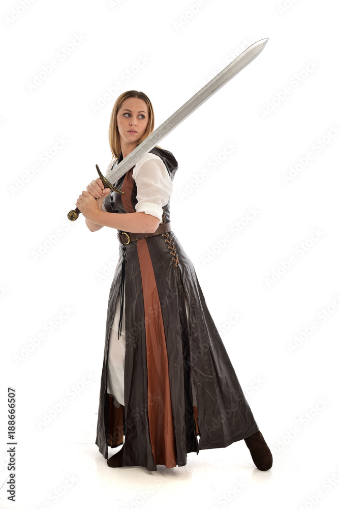 full length portrait of girl wearing brown fantasy costume, holding a sword. standing pose on white studio background. full length portrait of girl wearing brown fantasy costume, holding a sword. standing pose on white studio background.