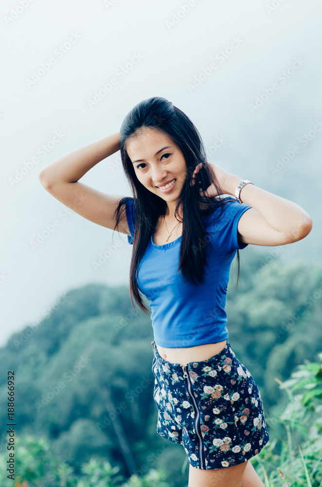 Asian young beautiful woman in a blue T-shirt on a cliff of a mountain in the fog