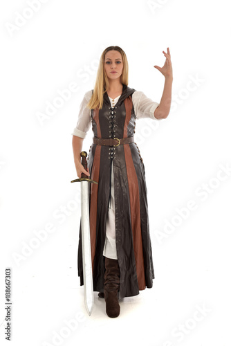 full length portrait of girl wearing brown fantasy costume, holding a sword. standing pose on white studio background. 