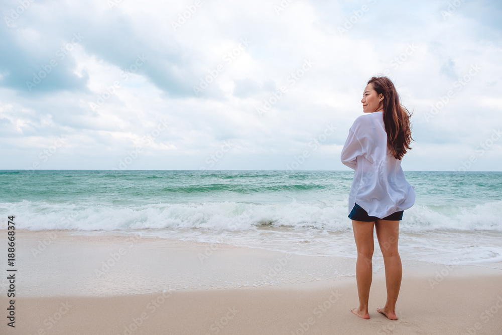 An Asian woman standing and looking at view on the beach with the sea and blue sky background An Asian woman standing and looking at view on the beach with the sea and blue sky background