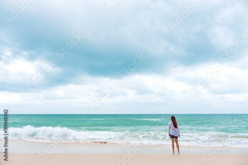 A woman standing and looking at view on the beach with the sea and blue sky background
