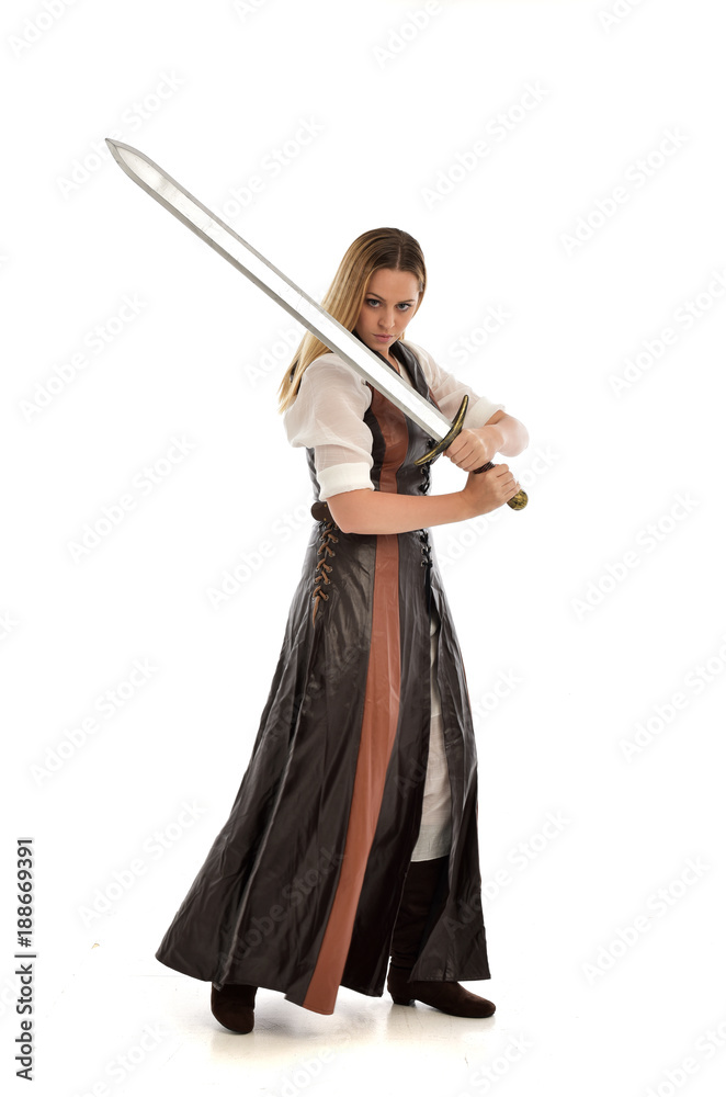 full length portrait of girl wearing brown fantasy costume, holding a sword. standing pose on white studio background. full length portrait of girl wearing brown fantasy costume, holding a sword. standing pose on white studio background.