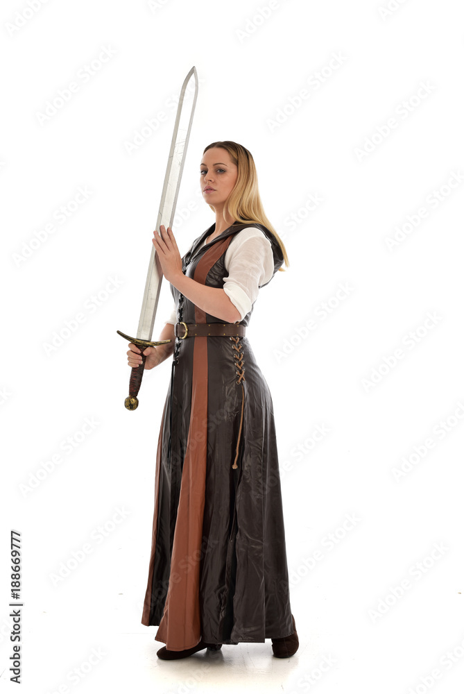 full length portrait of girl wearing brown fantasy costume, holding a sword. standing pose on white studio background. full length portrait of girl wearing brown fantasy costume, holding a sword. standing pose on white studio background.