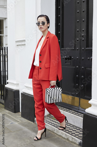 Chic young woman in red suit leaving smart London house