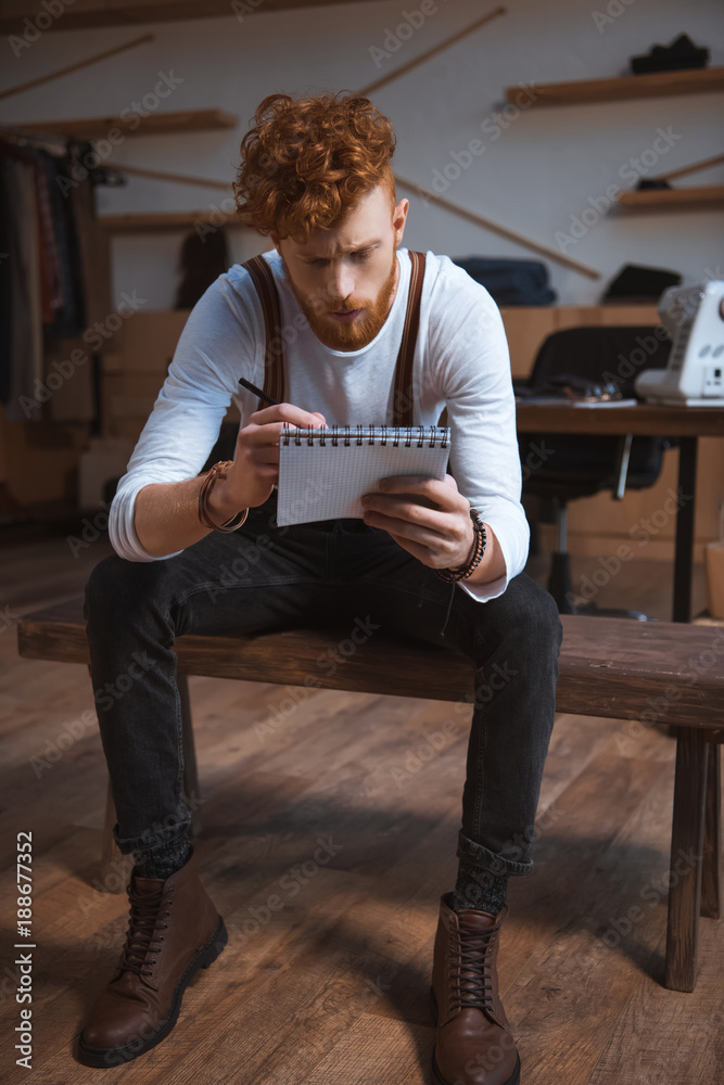 focused young male fashion designer taking notes in notepad at workplace