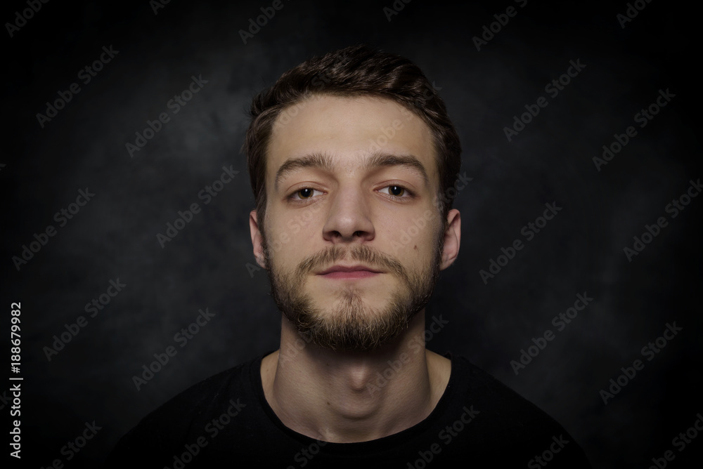 Portrait of a young man with a beard on a dark background.