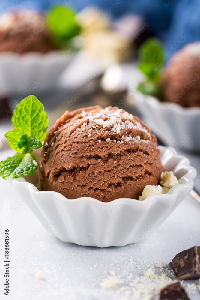 Chocolate ice cream scoop in white bowl with chopped white chocolate and mint decoration. Summer food concept with copy space.