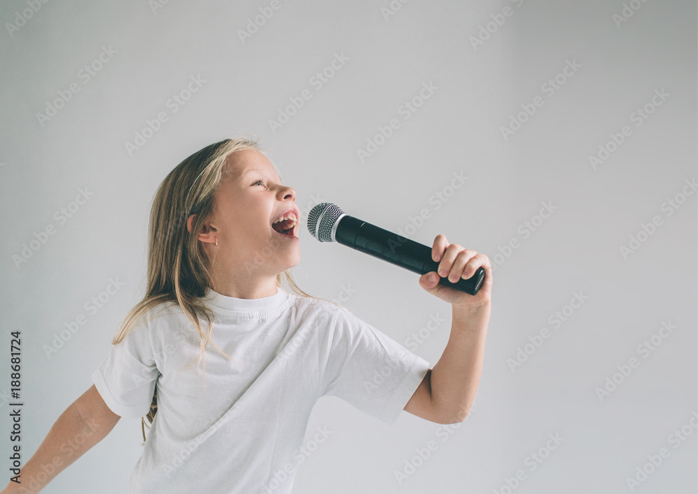 Girl Rocking Out. Image of a child singing to the microphone, isolated on light. Emotional portrait of an attractive kid on a gray background. Girl Rocking Out. Image of a child singing to the microphone, isolated on light. Emotional portrait of an attractive kid on a gray background.