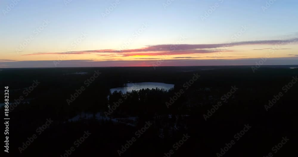 Sunset pond, Cinema 4k aerial view over a frosty forest and towards a frozen pond , on a sunny winter, evening dawn, in Raasepori, Uusimaa, Finland