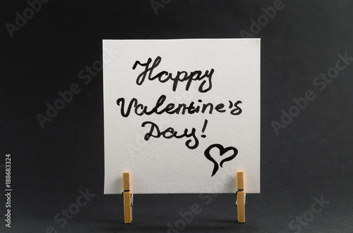 The sticker with the greeting happy Valentines day on the clothespin on a dark background.