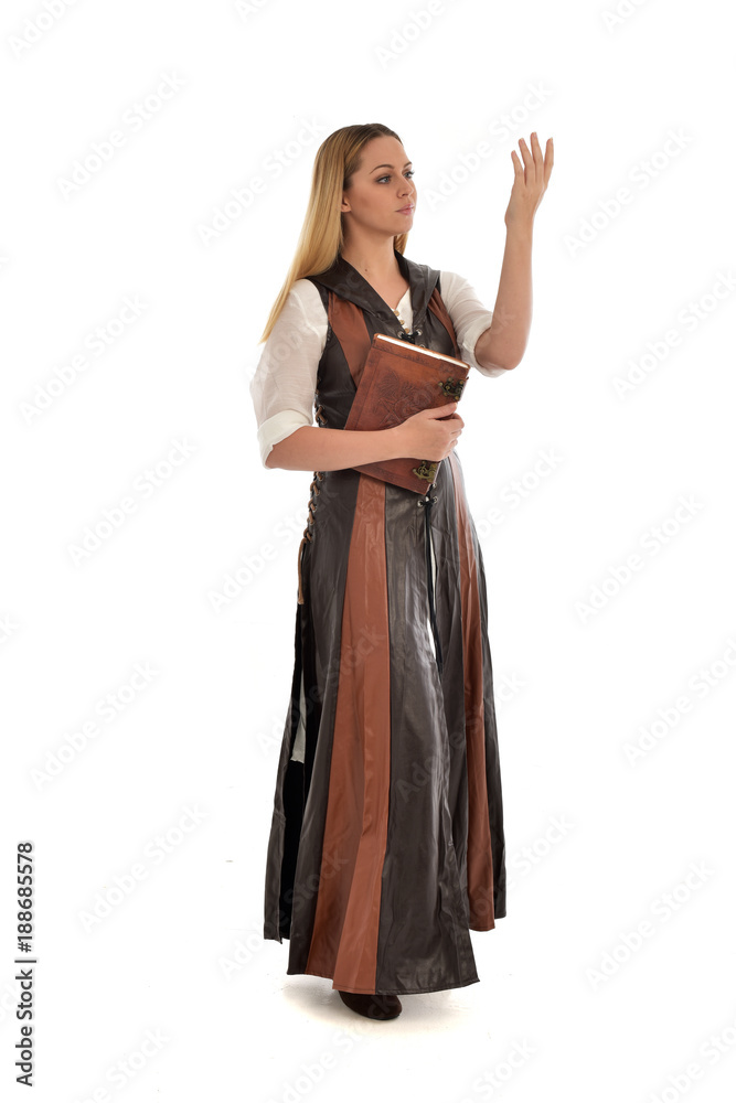  full length portrait of girl wearing brown  fantasy costume, holding a book. standing pose on white studio background. 