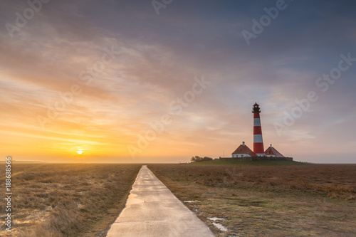 Sunrise at the lighthouse, a path seems to lead between the sun and lighthouse to infinity - lighthouse Westerhever, Germany