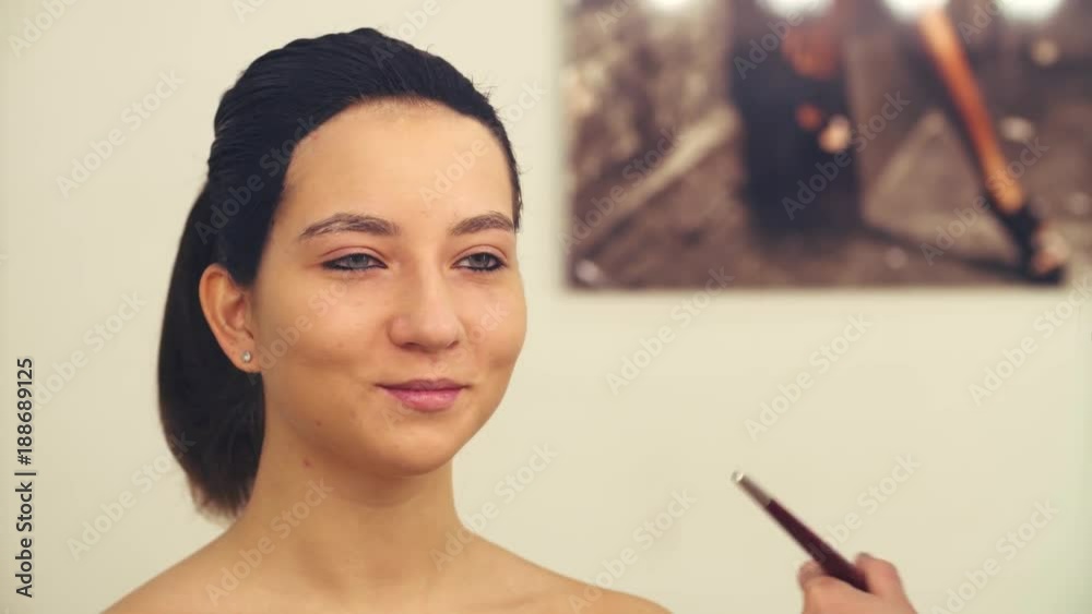 Face art. Professional makeup artist preparing to draw on the model's face. They talking. Model looking at herself in the mirror and smiling Face art. Professional makeup artist preparing to draw on the model's face. They talking. Model looking at herself in the mirror and smiling