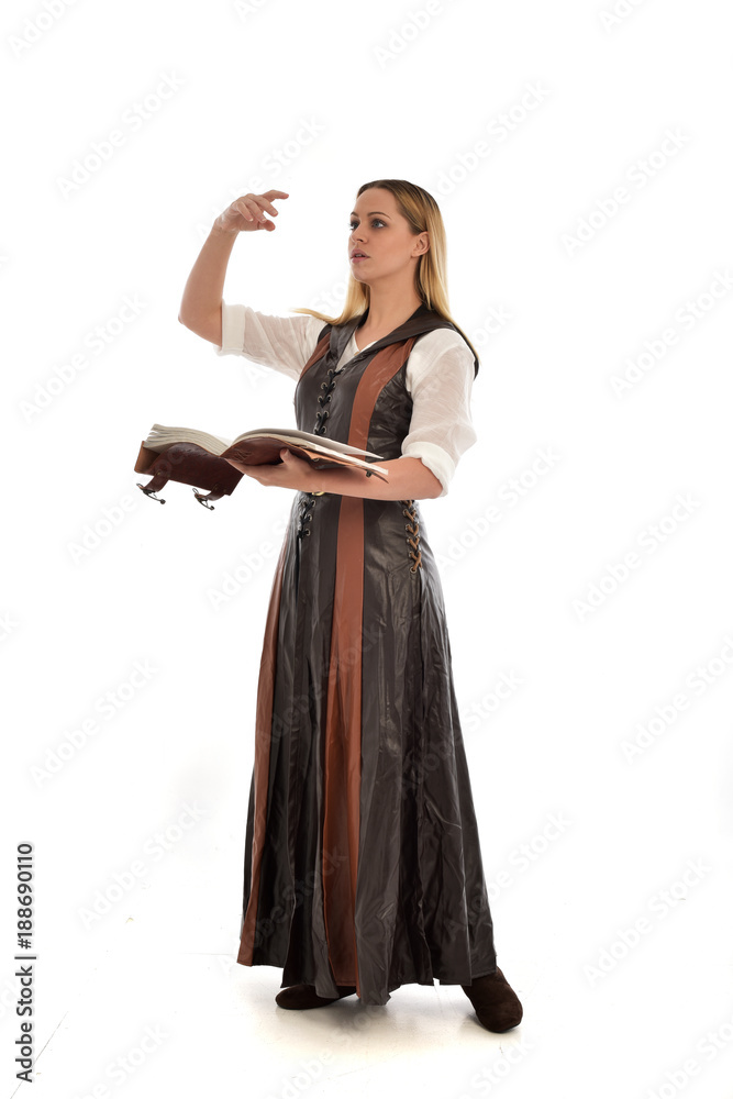  full length portrait of girl wearing brown  fantasy costume, holding a book. standing pose on white studio background. 