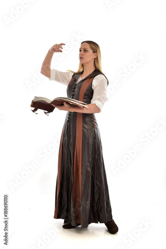  full length portrait of girl wearing brown fantasy costume, holding a book. standing pose on white studio background. 