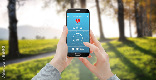 Girl checking her heart rate and steps on smartphone health app  while walking in park