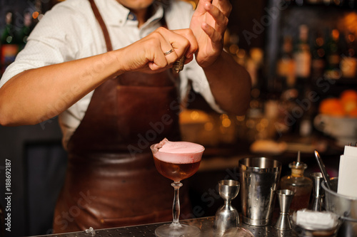 Barman in a brown leather apron making fruit alcoholic cocktail with foam
