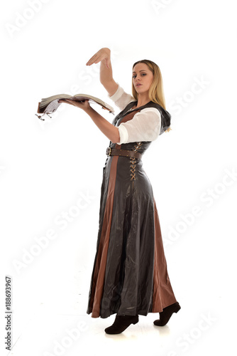  full length portrait of girl wearing brown fantasy costume, holding a book. standing pose on white studio background. 