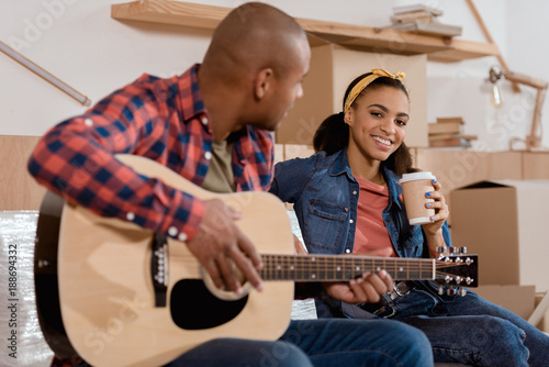 african american couple playing on acoustic guitar in new home with cardboard boxes