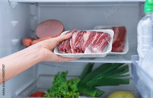 Bild auf Leinwand Woman putting raw meat in refrigerator, closeup