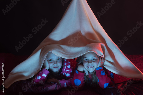 Girls with happy faces lie under pink blanket tent