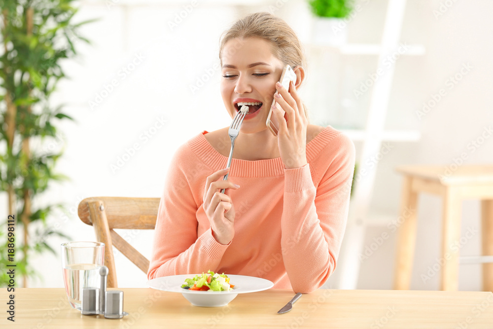 Young beautiful woman talking on phone while eating fresh salad at home