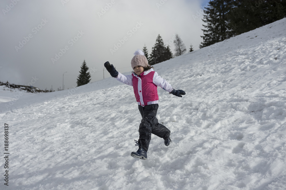 A  little girl is playng running on snowy slope. Negative space, copy space.