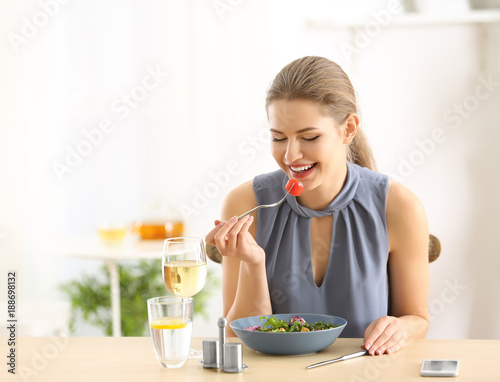 Young beautiful woman with glass of wine eating fresh salad at home