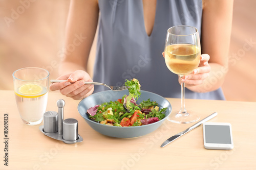 Young woman drinking wine and eating salad at table