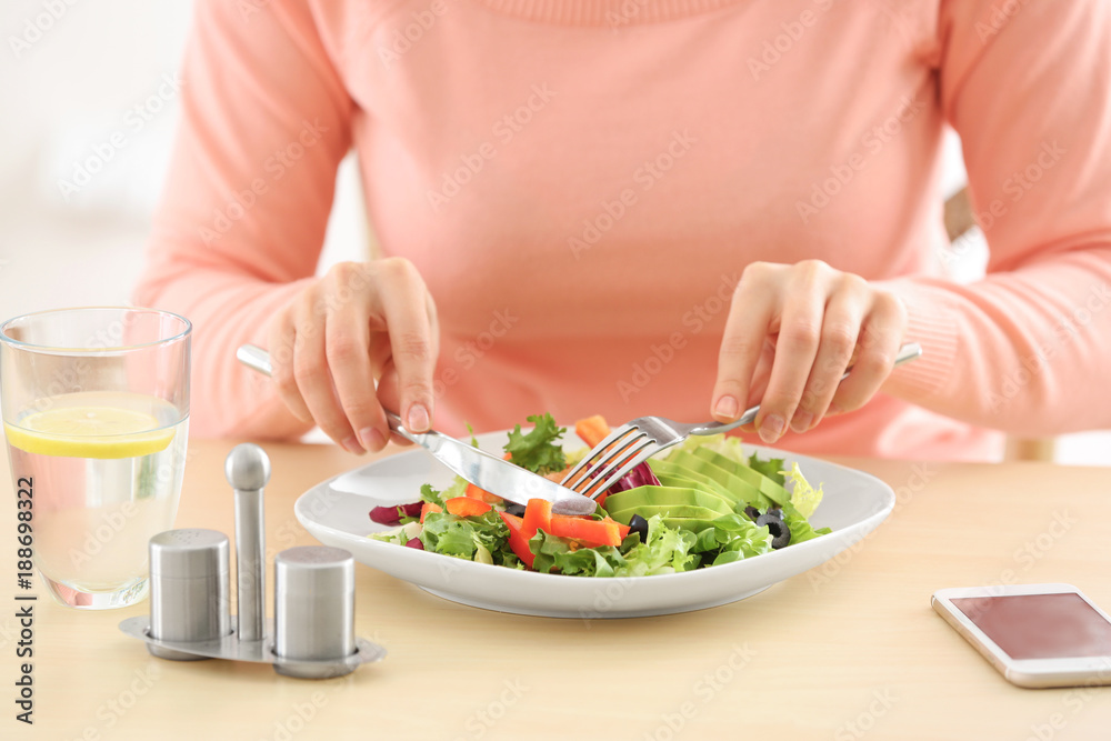 Young woman eating fresh salad at table