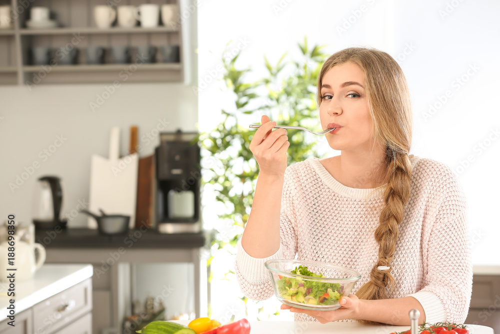 Young beautiful woman eating fresh salad in kitchen Young beautiful woman eating fresh salad in kitchen