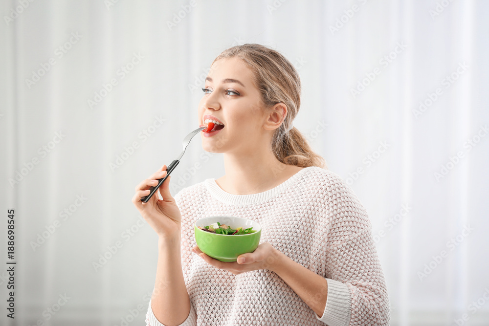 Young beautiful woman eating fresh salad on light background Young beautiful woman eating fresh salad on light background