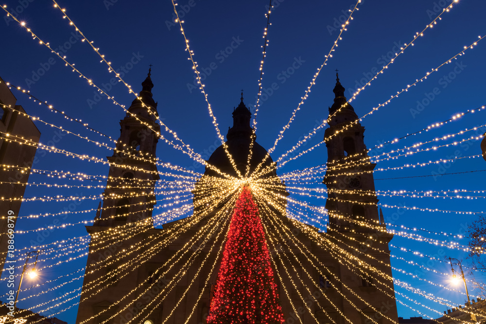 Fototapeta premium Lighting garland over Christmas tree against st. Stephen's Basilica outline in Budapest