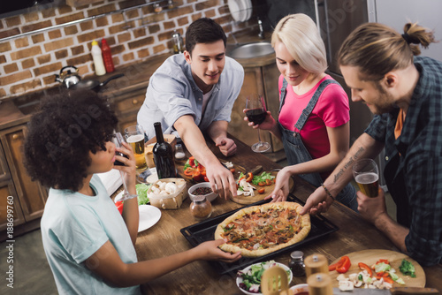 Canvas Print multicultural friends eating homemade pizza in kitchen