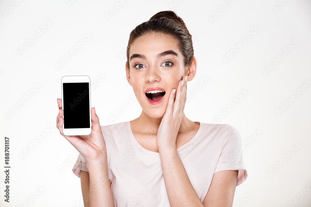 Portrait of successful brunette female 30s rejoicing her new modern smartphone showing it on camera over white wall Portrait of successful brunette female 30s rejoicing her new modern smartphone showing it on camera over white wall