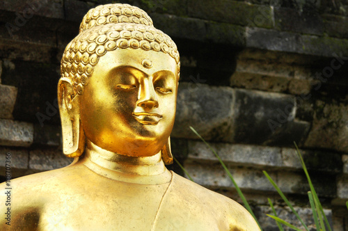 Closeup of Golden Buddha statue with temple wall in the background