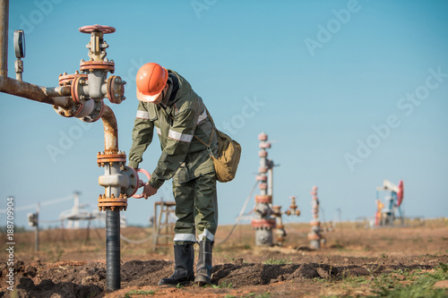 Oil worker is turning valve on the oil pipeline, oil deposit on the background. photo