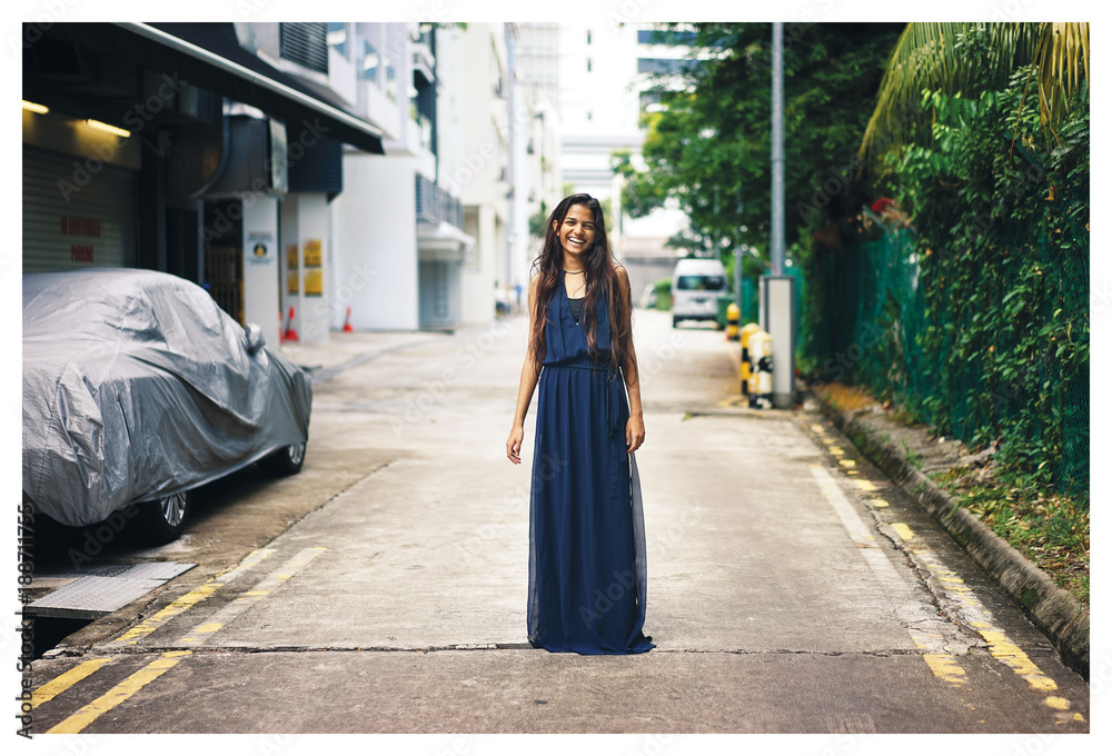 Portrait of young Indian Asian woman standing in the middle of the street wearing a long blue dress looking at the camera. 