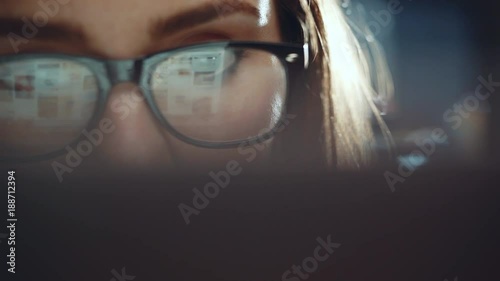 Closeup of attractive young woman looking at monitor while working at modern office and using laptop, hipster girl wearing glasses using computer touchscreen, closeup eyes photo