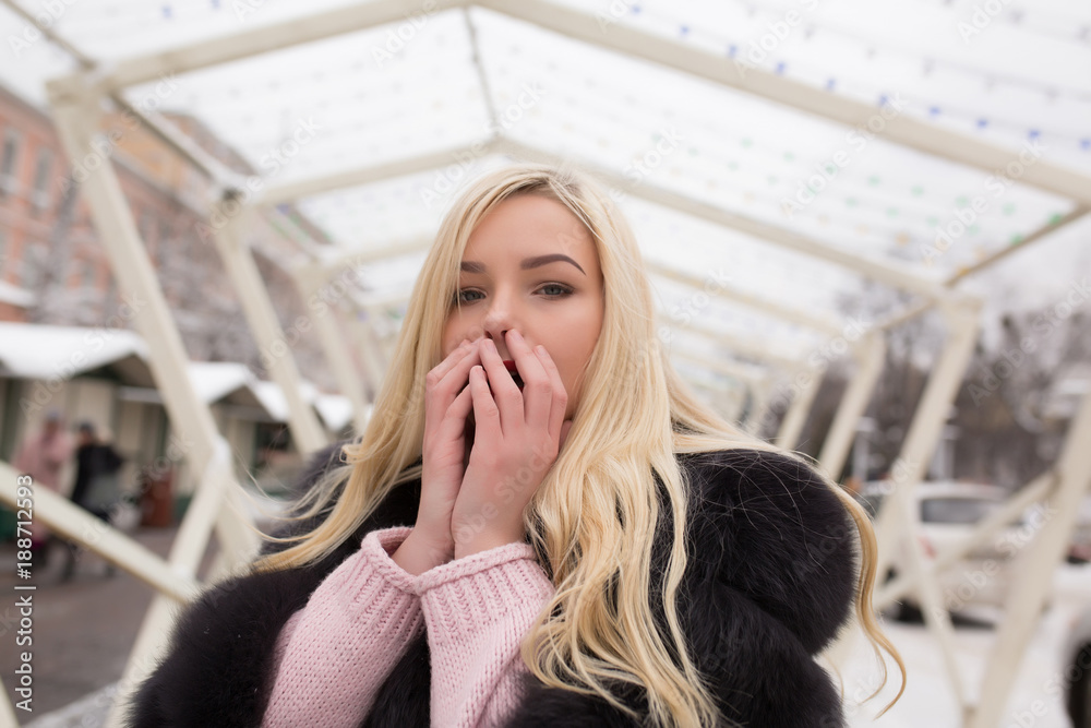 Outdoor portrait of attractive blonde woman warm her hands at the street in winter