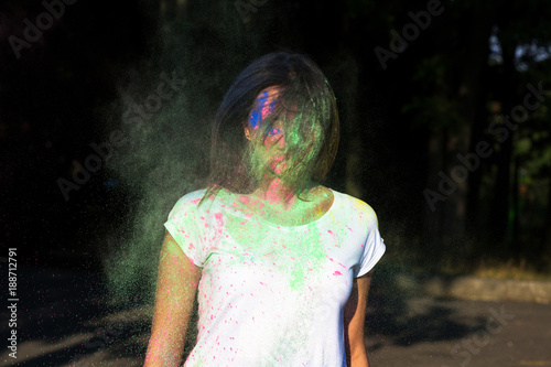 Closeup portrait of tanned woman posing with exploding green Holi powder in the park