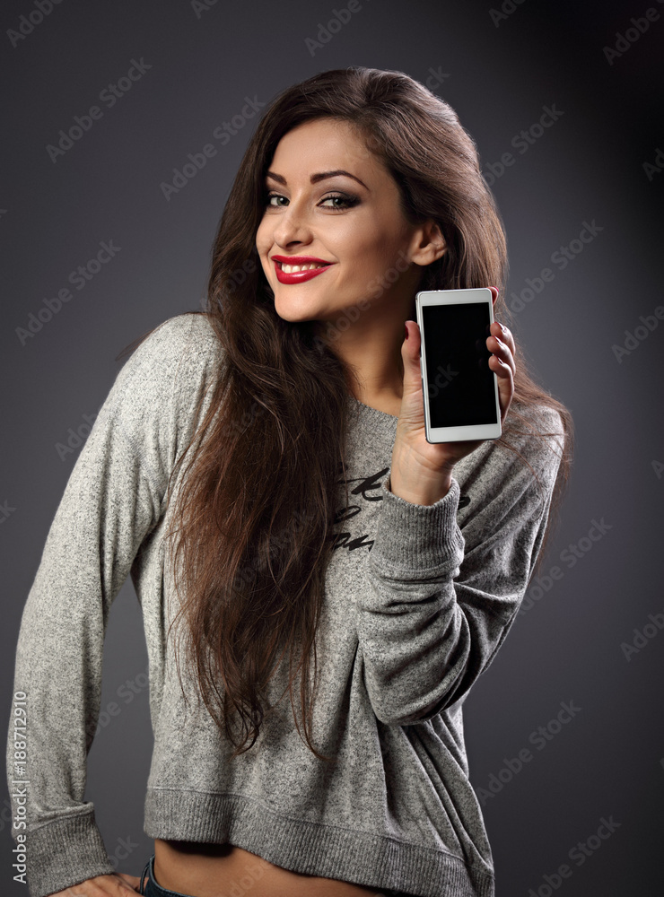 Happy smiling beautiful makeup woman holding and advertising mobile phone on grey dark background. Closeup portrait Happy smiling beautiful makeup woman holding and advertising mobile phone on grey dark background. Closeup portrait
