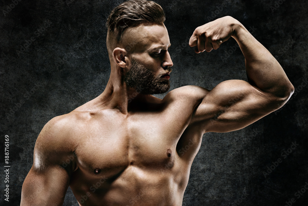 Athletic man showing his bicep. Photo of strong male with naked torso on dark background. Strength and motivation. Athletic man showing his bicep. Photo of strong male with naked torso on dark background. Strength and motivation.