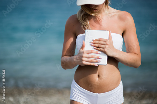 Young beautiful woman in sport suit is using her tablet on the beach