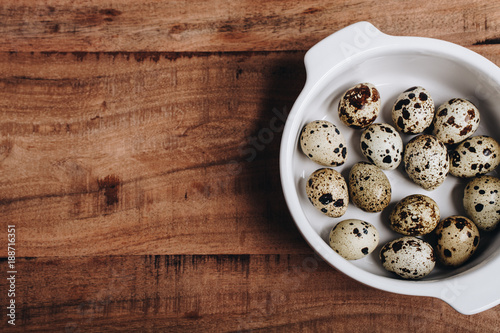Quail eggs in white bowl, wooden background